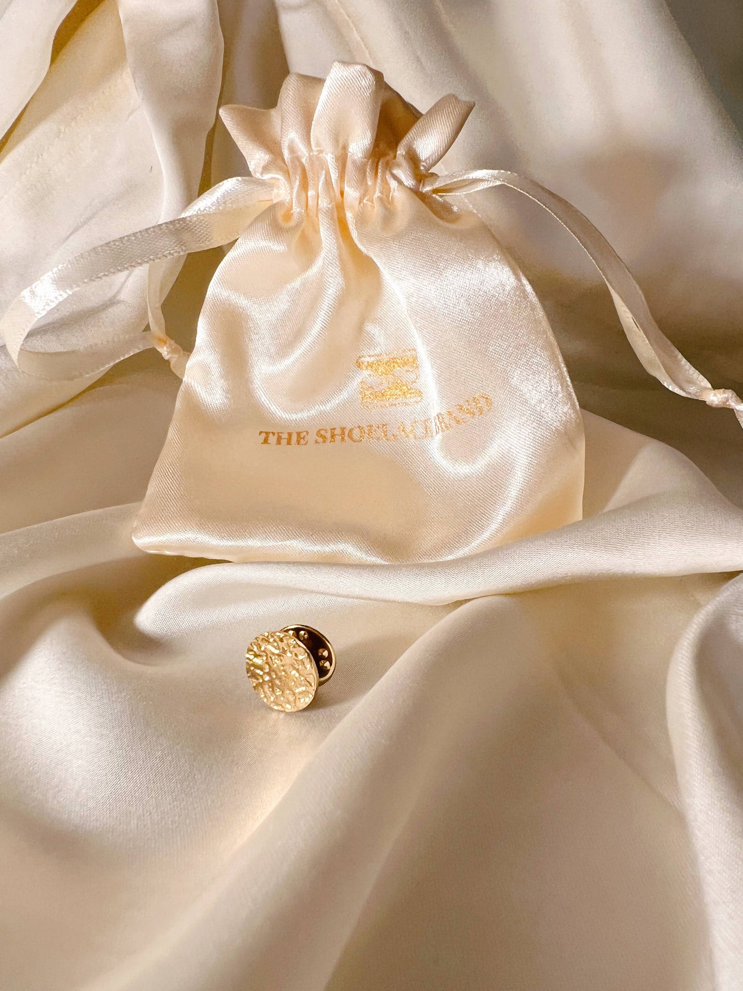 The Shoelace Brand Gold Textured Pin -pinssi nappikorupohjalla