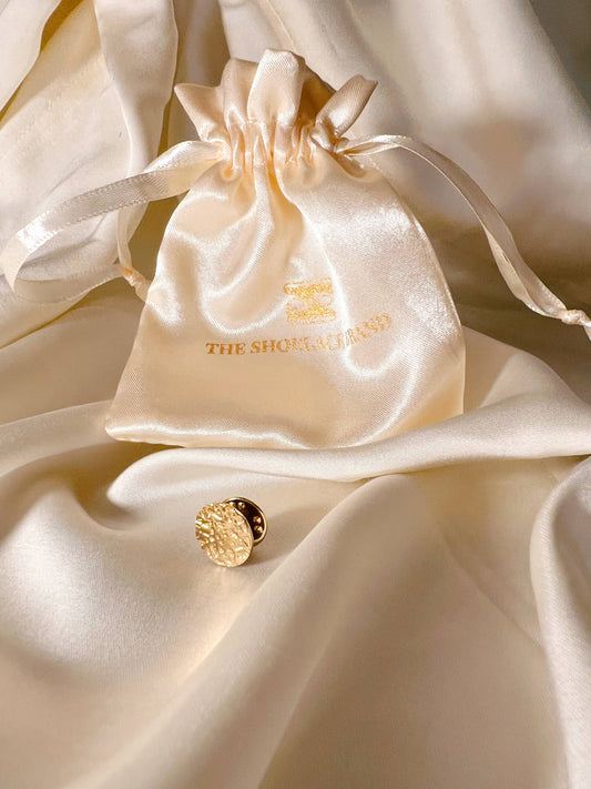 The Shoelace Brand Gold Textured Pin -pinssi nappikorupohjalla